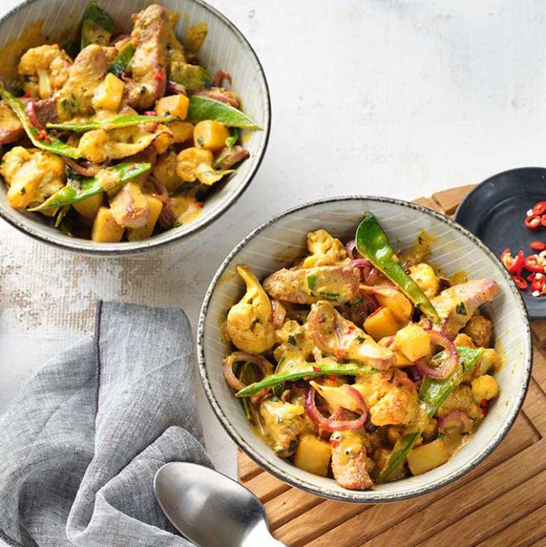 Zwei Schalen mit Puten-Curry, die aromatisch gewürzt sind und mit frischen Zutaten angerichtet wurden.