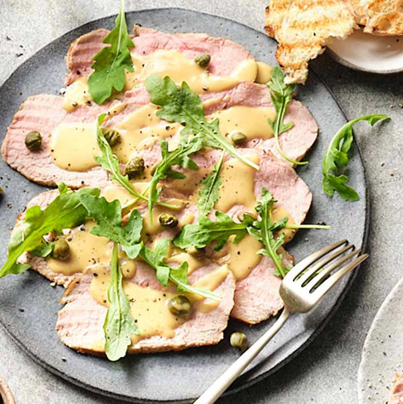 Vitello tonnato auf einem Teller angerichtet, garniert mit Kapern und frischen Kräutern, appetitlich präsentiert.