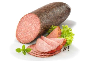 Produktaufnahme von Pfeffersalami auf neutralem Hintergrund, luftgetrocknete Rohwurst mit sichtbaren Pfefferkörnern auf der Oberfläche, tiefrote Fleischfarbe, grobkörnige Textur, handwerklich hergestellte Salami
