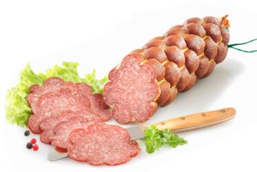 Produktaufnahmen von Lammsalami auf neutralem Hintergrund, luftgetrocknete Rohwurst, feine und grobe Fleischstruktur sichtbar, tiefrote Farbe, traditionelle handwerkliche Wurst, hochwertige Lammsalami