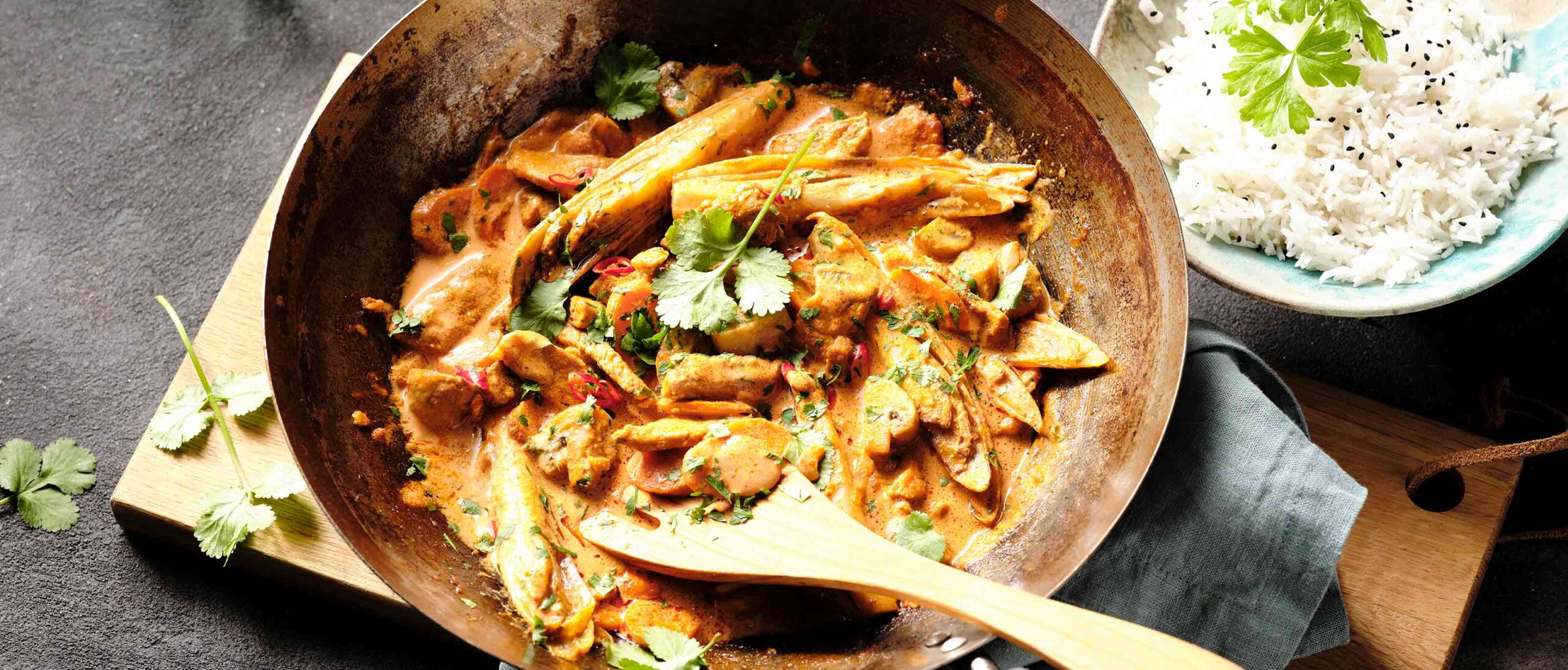 Pfanne mit Schweinecurry und Holzlöffel, der die köstliche Mahlzeit ansprechend präsentiert.