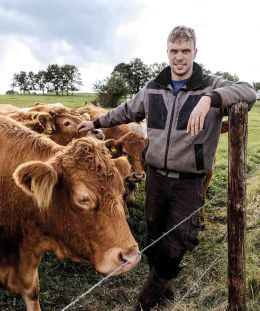 Landwirt schaut in die Kamera, umgeben von seinen Rindern auf der Weide.