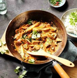 Pfanne mit Schweinecurry und Holzlöffel, der die köstliche Mahlzeit ansprechend präsentiert.